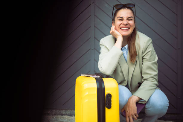 istock A smiling woman crouches leaning on her yellow suitcase. Copy space. 1439054624