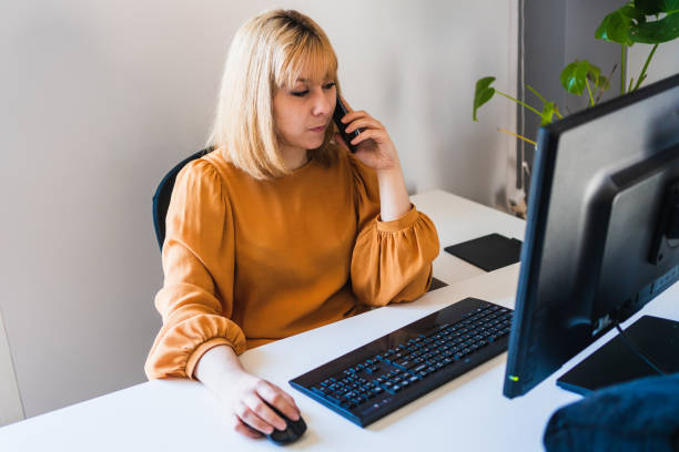 istock Woman working talking on her smartphone in front of a desktop computer in the office 1439056102