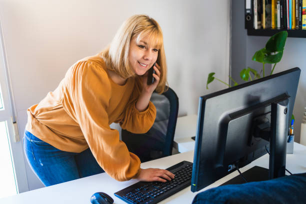 istock Smiling working woman standing at desktop computer in office 1439056410