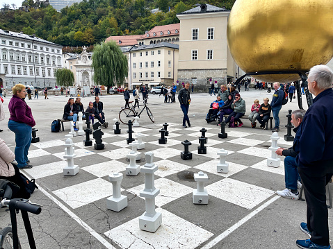 Salzburg, Austria - September 30, 2022: An audience gathers as people actively play chess on a giant chess board below the golden sculpture called Sphaera.