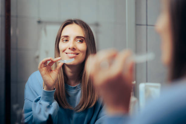 mujer quitándose el retenedor transparente en el espejo del baño - young women smiling women human teeth fotografías e imágenes de stock