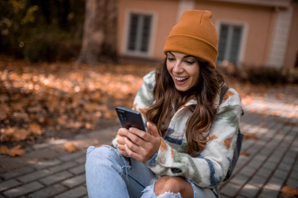 istock Cheerful young woman sitting on skateboard and using smartphone 1439067869