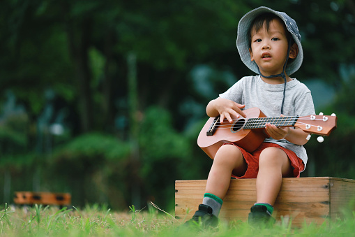 Portrait of an Asian young boy in leisure activity, playing ukulele at local park.