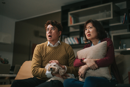 Asian Chinese couple watching scary movie at home in living room during weekend night