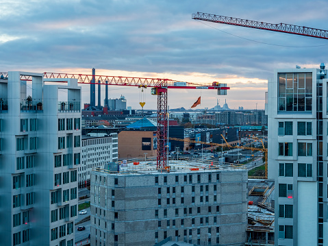 Copenhagen, Denmark - Oct 20, 2018: Construction cranes for new building, surrounded by apartment flats. Morning view over city skyline from elevated vantage point. Modern European buildings around.