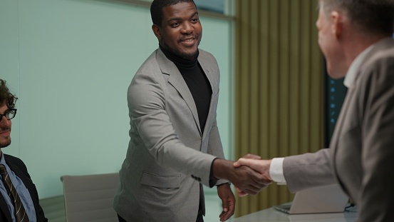 Business people shacking hands together showing successful contract agreement beside secretary business officer clapping hands with gladness in comfortable meeting room