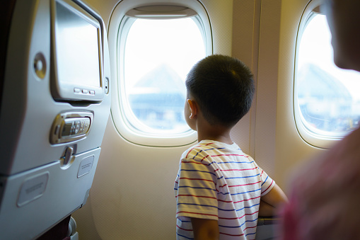 Asian children look at the aerial view of the sky and clouds outside the plane window while sitting on the plane seat.