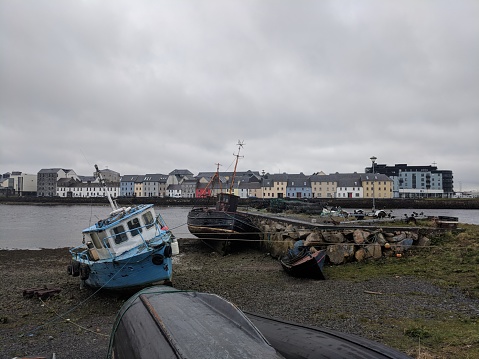 Blue boat sits along the shore in Galway with colorful homes along the waterfront.