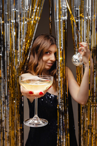 New Year's eve party concept. Woman holding a glass of champagne, festive shiny decor, focus on the glass