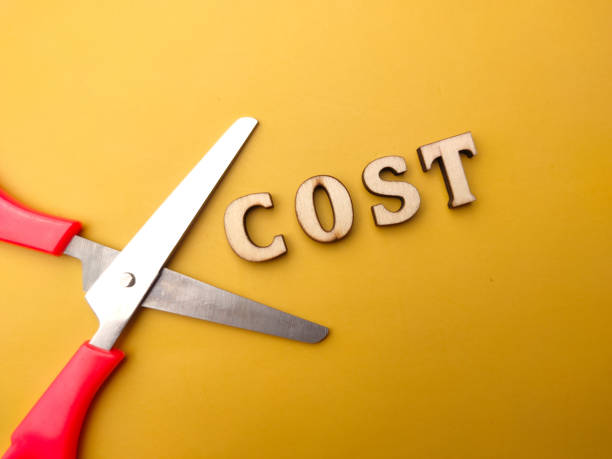 istock Scissors and wooden word with text COST on a yellow background. 1439112218