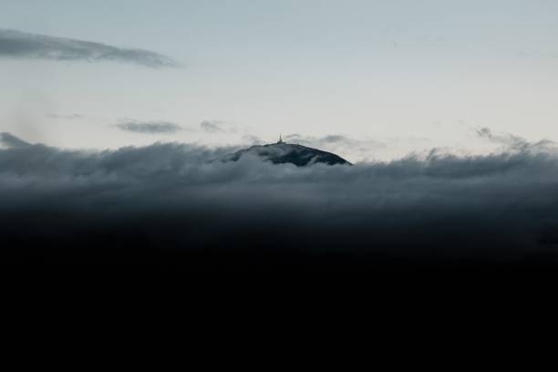 A hill covered in dark heavy clouds under a pale sky at daytime