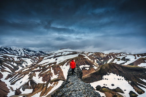 Hiker man standing on the peak with volcanic mountain range with snow covered on Blanhjukur trail in summer at Landmannalaugar, Iceland