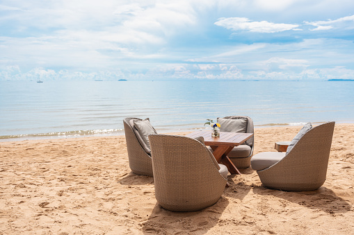 Rattan chair with pad and table setting on the beach by tropical sea on sunny day
