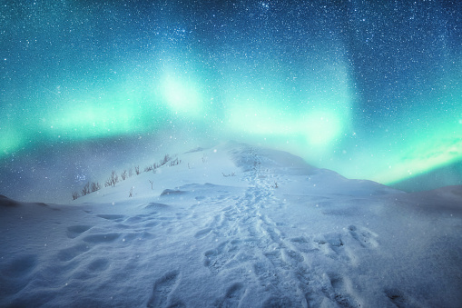 Scenery of Aurora borealis over snowy hill with footprint and snowing on the peak of mountain in wintertime