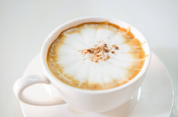 Stock photo showing close-up view of restaurant breakfast with a white coffee cup and saucer of frothy cappuccino coffee that has sprinkled cocoa powder on the milk foam.