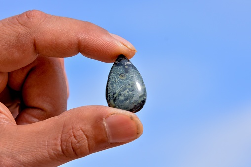 A closeup shot of a man holding a teardrop shape stone with a clear blue sky in the background