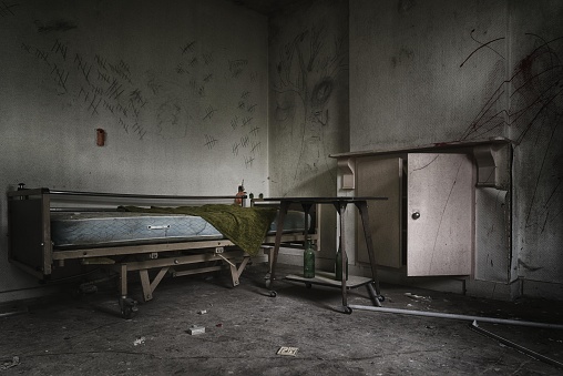 A dramatic shot of an abandoned prison room with a broken bed and weathered windows