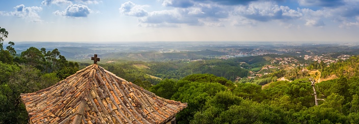 A panoramic shot of the Bucaco forest as seen from above with an old chapel roof in the foreground