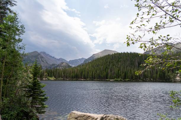 istock Lake surrounded by lush green dense forests under blue cloudy sky 1439133796