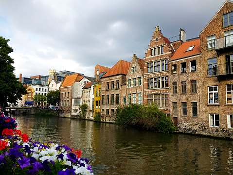 The buildings surrounded by the river and flowers under a cloudy sky in Ghent in Belgium
