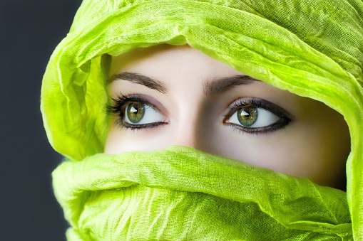 A closeup of the eyes of a woman with a green hijab under the lights against a grey background