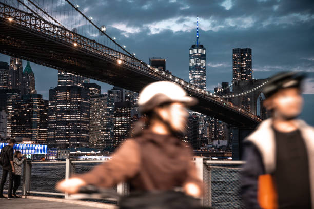 People walking on riverside walkway in Brooklyn Bridge park with Lower Manhattan downtown skyscrapers and Brooklyn Bridge on the background.