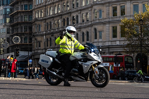 London, United Kingdom – November 11, 2019: British police officer on motor bike stops car traffic at busy trafalgar square intersection for government escort. London traffic needs to stop