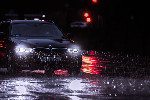 Munich, Germany – June 27, 2019: Heavy rainstorm in munich city night time car driving by in lots of rain water reflecting in light