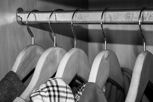 Hangers with clothes hang in the closet. Black and white photo of a hanger in a closet with clothes. Things hang on wooden hangers.