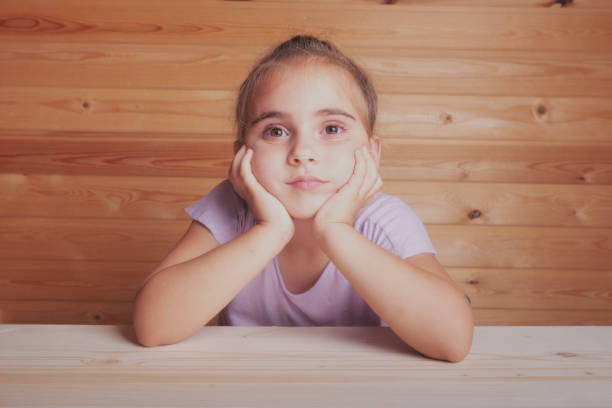 sad little girl thoughtful sit , propping up face with her hands. close-up face, side view with copy-space