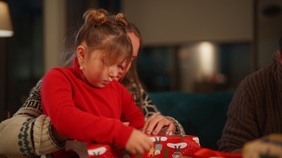 A young mother and her small daughter are preparing Christmas presents in the living at home at night.