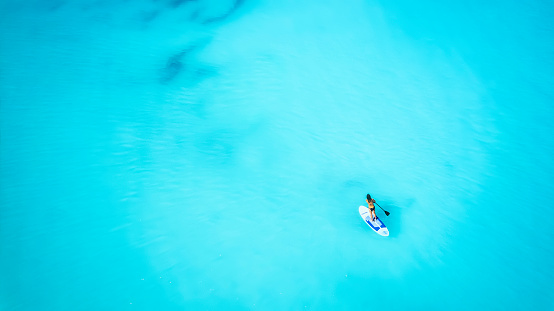 Aerial top down view of a woman on a stand up paddle (SUP) board over the turquoise Caribbean ocean in the Bahamas islands