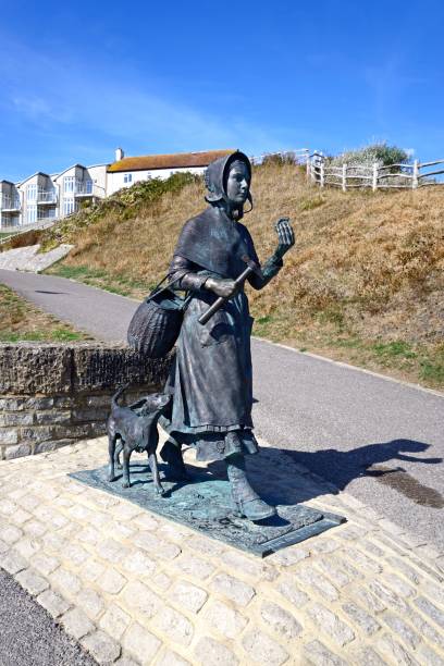 A bronze statue depicts a woman gently holding a child's hand, standing on a memorial stone. The serene cemetery features vibrant autumn colors, creating a tranquil atmosphere.