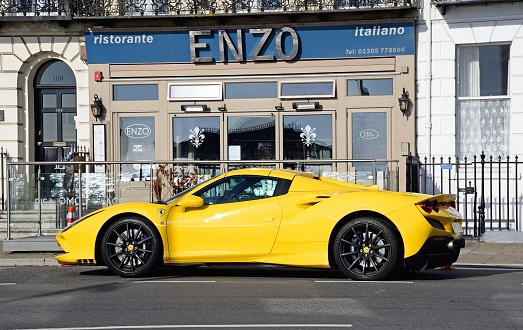 A bright yellow Ferrari F8 Spider parked outside the Enzo restaurant along the promenade, Weymouth, Dorset, UK, Europe.