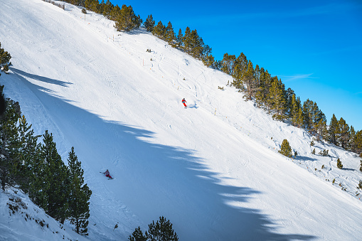 Couple of skiers skiing down the steep piste, one crashing, in Pyrenees Mountains. Winter ski holidays in El Tarter, Grandvalira, Andorra