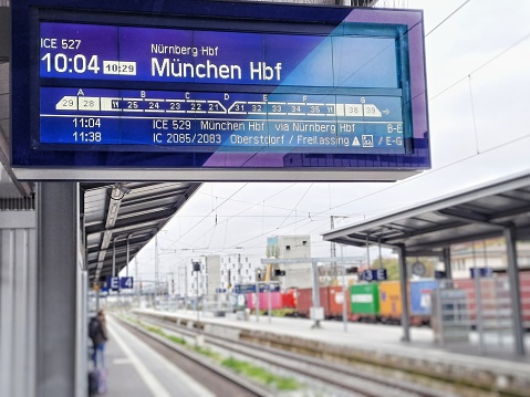 Munich, Germany - November 05, 2022: Blue departure sign on the platform in Würzburg to Munich with waiting passengers in the background.