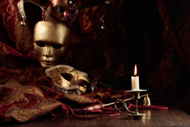 istock Burning candle in an old brass candlestick and carnival masks. 1439161583
