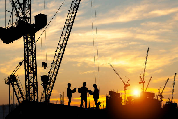 silhouette of engineer and worker team on building site, construction site at sunset in evening time - construction imagens e fotografias de stock