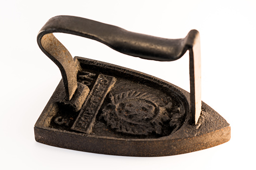 Close up on a old heavy cast iron ironing, isolated on white background. Beautiful vintage object to heat on a stove.