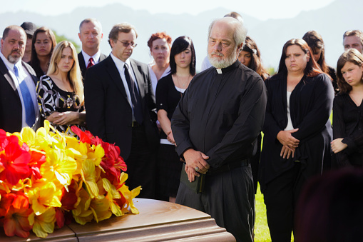 A priest standing graveside at a funeral.