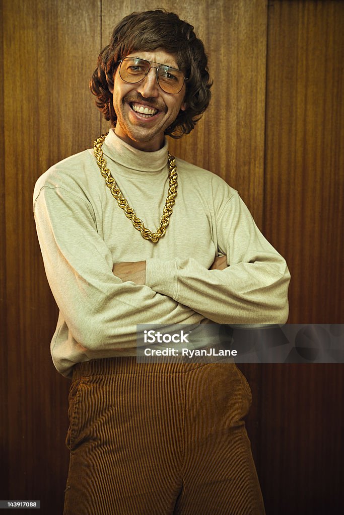 Bling Retro Mustache Man A smiling goofy man from the 1970s - 1980s poses for a picture in his turtleneck, high waisted elastic corduroy pants, and his fancy gold chain necklace .  Classy tinted glasses and suave mustache.  Wood panel wall in the background. 1980-1989 Stock Photo