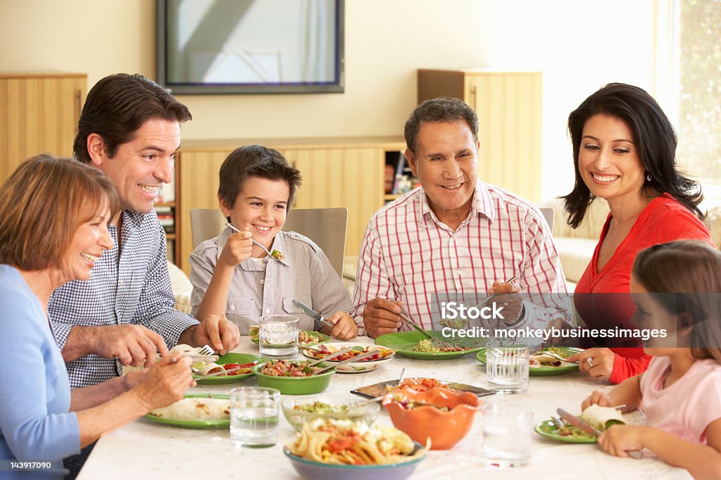 Extended Hispanic Family Enjoying Meal At Home Extended Hispanic Family Enjoying Meal Sitting At Dinner Table At Home Family Stock Photo