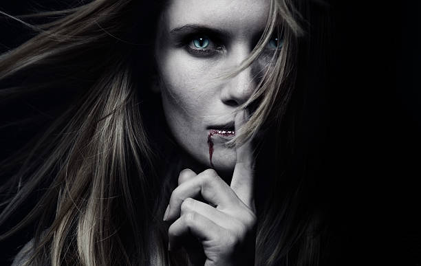 A female vampire with blood dripping Portrait of a female vampire with long hair over black background. She has cat's eyes.  Finger on Lips. Halloween vampire woman stock pictures, royalty-free photos & images