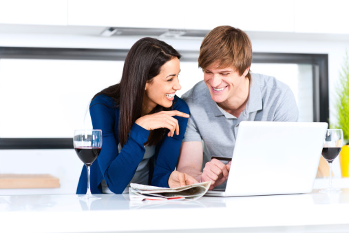 Couple in modern kitchen shopping online with credit card, laptop and road map.