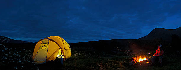 Wilderness camp fire child toasing marshmallows Scotland Child toasting marshmallows over open camp fire beside an illuminated yellow dome tent beneath the silhouetted mountain peaks of Glen Coe, Scotland. ProPhoto RGB profile for maximum color fidelity and gamut. buachaille etive mor photos stock pictures, royalty-free photos & images