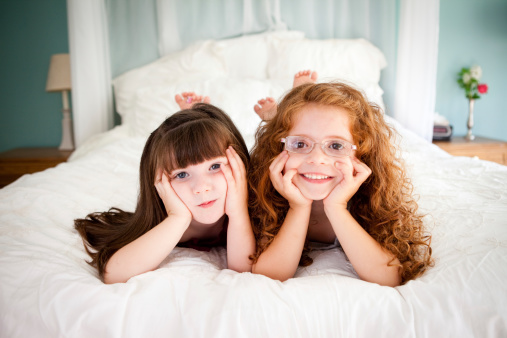 Color image of  two happy, adorable sisters lying together on the bed in a teal bedroom at home.