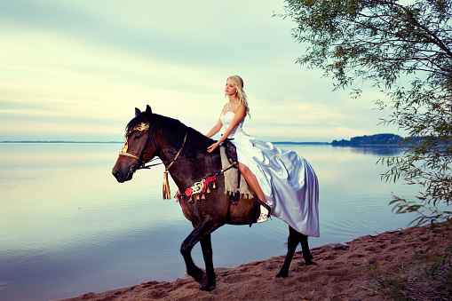 Bride with white dress on horse near lake looking away , fantasize