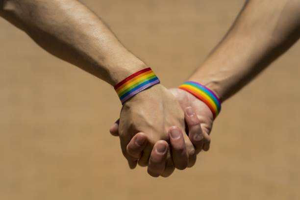 istock Two Caucasian men holding hands with a rainbow-patterned wristband against a brown background 1439178232