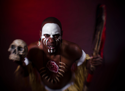 closeup of a creepy bald evil clown, standing in front of a dirty and old circus tent, wearing a gray costume with a white ruff, and starring at the observer with a frightening smile