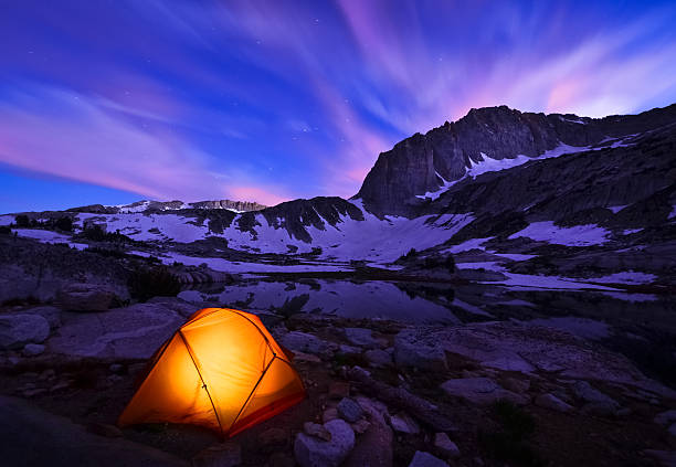 Illuminated yellow tent on snowy mountains range at night stock photo